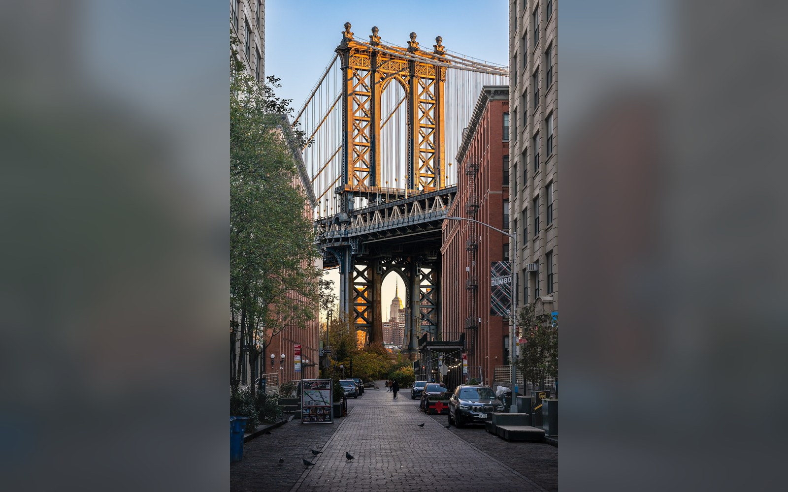 A cobbled street between brick warehouses with the Manhattan Bridge framed at the end